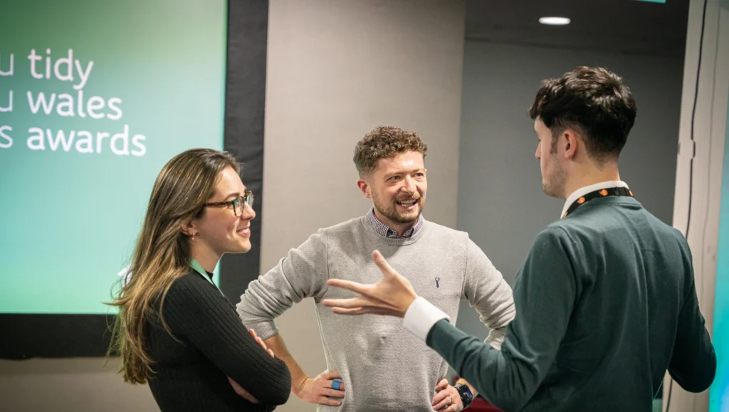 Three people standing in a room, one has their back turned to the camera, and the other two are standing and smiling.